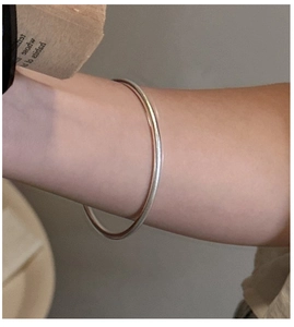 Macro shot of minimalist silver polished thin bangle on female wrist with glossy finish