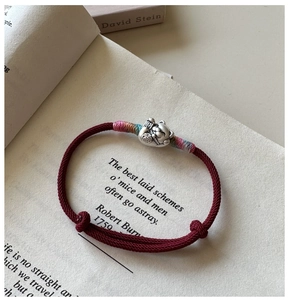 Gros plan sur un bracelet tressé rouge avec pendentif chat porte-bonheur en argent