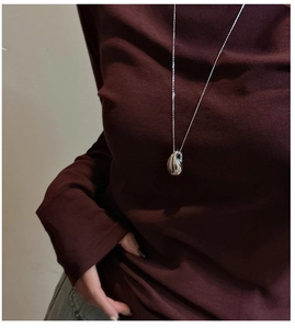 Détail du collier pendentif goutte d'argent minimaliste sur un vêtement bordeaux