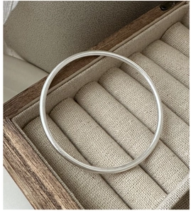 Close-up of minimalist matte S925 silver bangle inside a beige fabric jewelry box