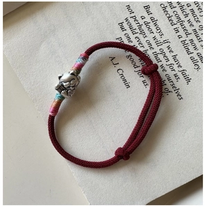 Gros plan du bracelet tressé rouge avec breloque chat Maneki-neko en argent sur un livre