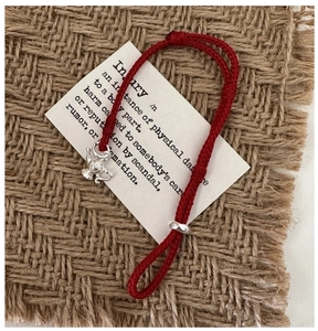 Macro detail of red woven cord bracelet with silver teapot charm on rustic linen background