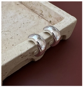 Detailed view of polished S925 silver C-shape hoop earrings on a textured stone tray