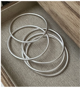 Macro shot of five matte S925 sterling silver minimalist bangles on a linen background