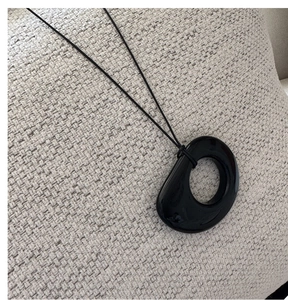 Close-up of a minimalist black irregular geometric pendant with polished finish on woven fabric