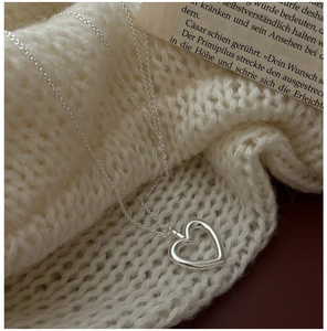Macro view of hollow heart pendant necklace on white knit sweater with vintage book