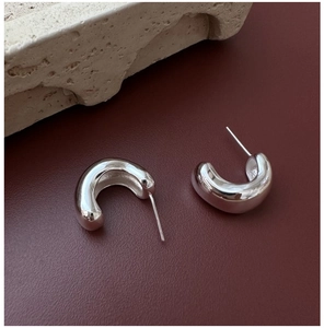 Macro detail of polished S925 sterling silver C-shaped hoop earrings on leather background