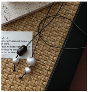 Detailed macro view of silver brushed beads and brown barrel bead on a long cord necklace