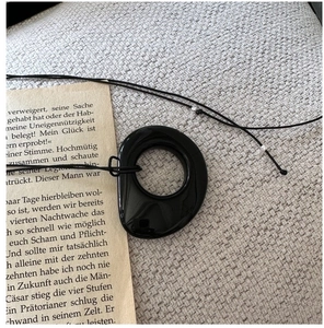 Close-up of irregular black obsidian ring pendant on rope chain over book pages