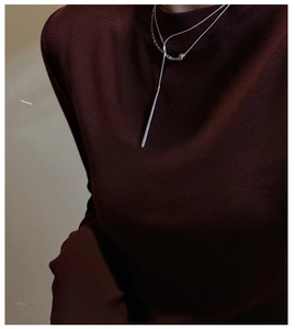 Close-up of a minimalist silver vertical bar pendant on a dark red sweater texture