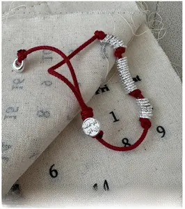 Detail of red braided rope bracelet with silver rings and round pendant on canvas