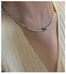 Detail of silver beaded necklace with turquoise accents worn over a beige sweater