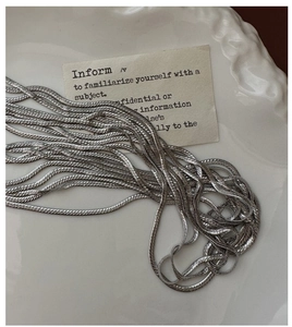 Detailed view of multiple silver S925 flat snake chains on a ceramic plate