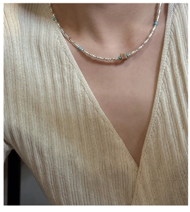 Close-up of S925 silver beaded necklace with turquoise accents on a beige knit cardigan
