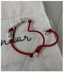 Close-up of red braided rope bracelet with silver hammered beads on burlap background