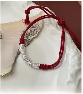 Detailed shot of woven red rope bracelet with hammered silver rings on vintage paper