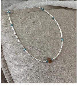 Detail of S925 silver beaded necklace with turquoise and brown square beads on fabric