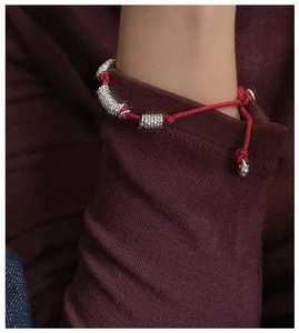 Detail of red braided rope bracelet with silver spiral metal beads on wrist