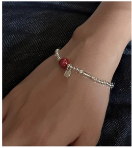 Macro detail of S925 sterling silver beaded bracelet with red bead and Fu tag on wrist