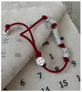 Detailed view of red woven S925 silver bracelet with textured beads on linen background