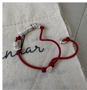Macro detail of red woven rope bracelet with silver rings on a textured canvas bag