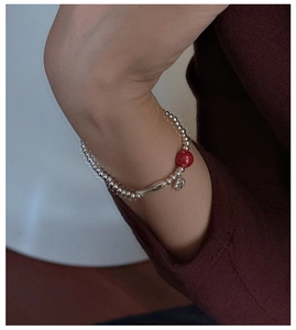 Detailed view of S925 silver beaded bracelet with red bead and fish charm on wrist