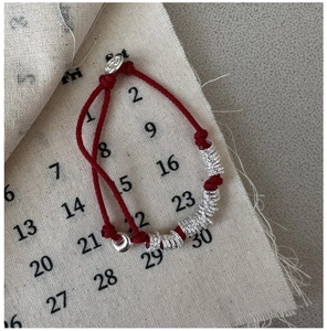 Close-up of red braided rope bracelet with S925 silver textured rings and round charm