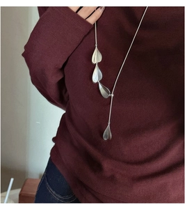 Detail of silver long sweater necklace featuring multiple brushed leaf pendants on a red knit
