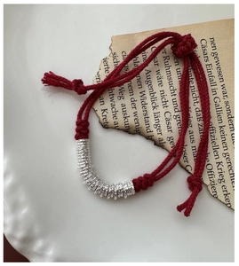 Macro detail of red woven rope bracelet with hammered silver rings on vintage paper