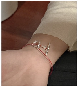 Macro shot of minimalist S925 silver OT clasp on a braided red rope bracelet worn on wrist