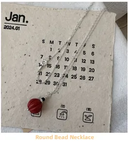 Détail d'un collier en argent S925 avec une perle de cinabre rouge texturée sur fond papier