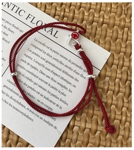 Macro detail of red woven bracelet with silver beads and enamel smiley face charm