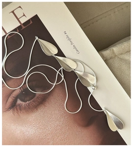 Detail of silver snake chain necklace with matte leaf pendants over an artistic magazine