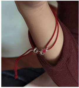 Close-up of minimalist red woven bracelet with silver smile charm on a woman's wrist