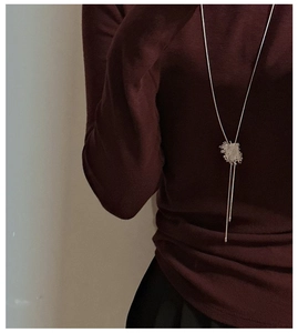 Dettaglio di una collana lunga argentata con ciondolo quadrato su tessuto bordeaux