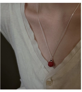 Gros plan du collier en argent S925 avec pendentif citrouille rouge sur gilet beige