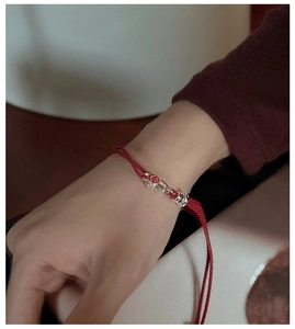 Close-up of a red woven rope bracelet with a silver red enamel smiley face charm