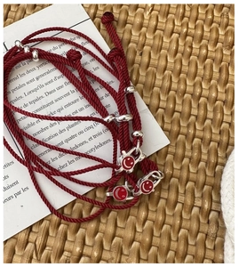 Detail of red braided S925 silver smile face bracelets on minimalist paper backdrop