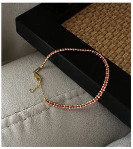 Close-up of minimalist handmade red braided bracelet with gold beads and lobster clasp detail