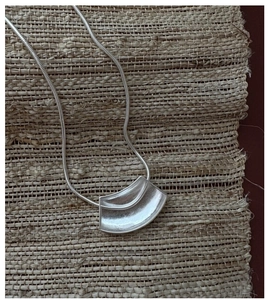 Détail de la chaîne serpent argentée et du pendentif géométrique sur un support tressé