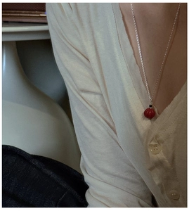 Détail d'un pendentif perle citrouille rouge sur une fine chaîne argentée femme