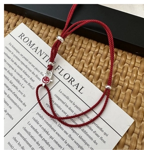 Detail of red braided silver bracelet with metal beads and a circular smiley face charm