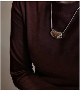 Gros plan d'un collier pendentif argenté incurvé sur un pull en maille rouge foncé