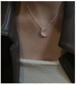 Macro detail of crescent moon pendant with hammered texture and fine bead chain