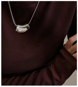 Détail d'un pendentif argenté courbé avec une chaîne serpent sur un fond en tricot rouge