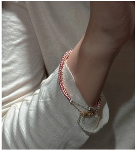 Close-up of a handmade red bead bracelet with a gold clasp on a beige knit sleeve