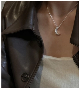 Detail of silver moon pendant on beaded chain worn over dark leather jacket