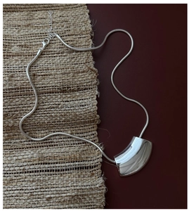 Détail macro du pendentif argenté incurvé sur une chaîne serpent minimaliste