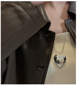Makroaufnahme einer 3D-Herz-Halskette in Silber auf einer Lederjacke im Vintage-Stil