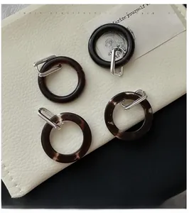 Detail of S925 sterling silver buckle and dark brown resin hoop earrings on leather